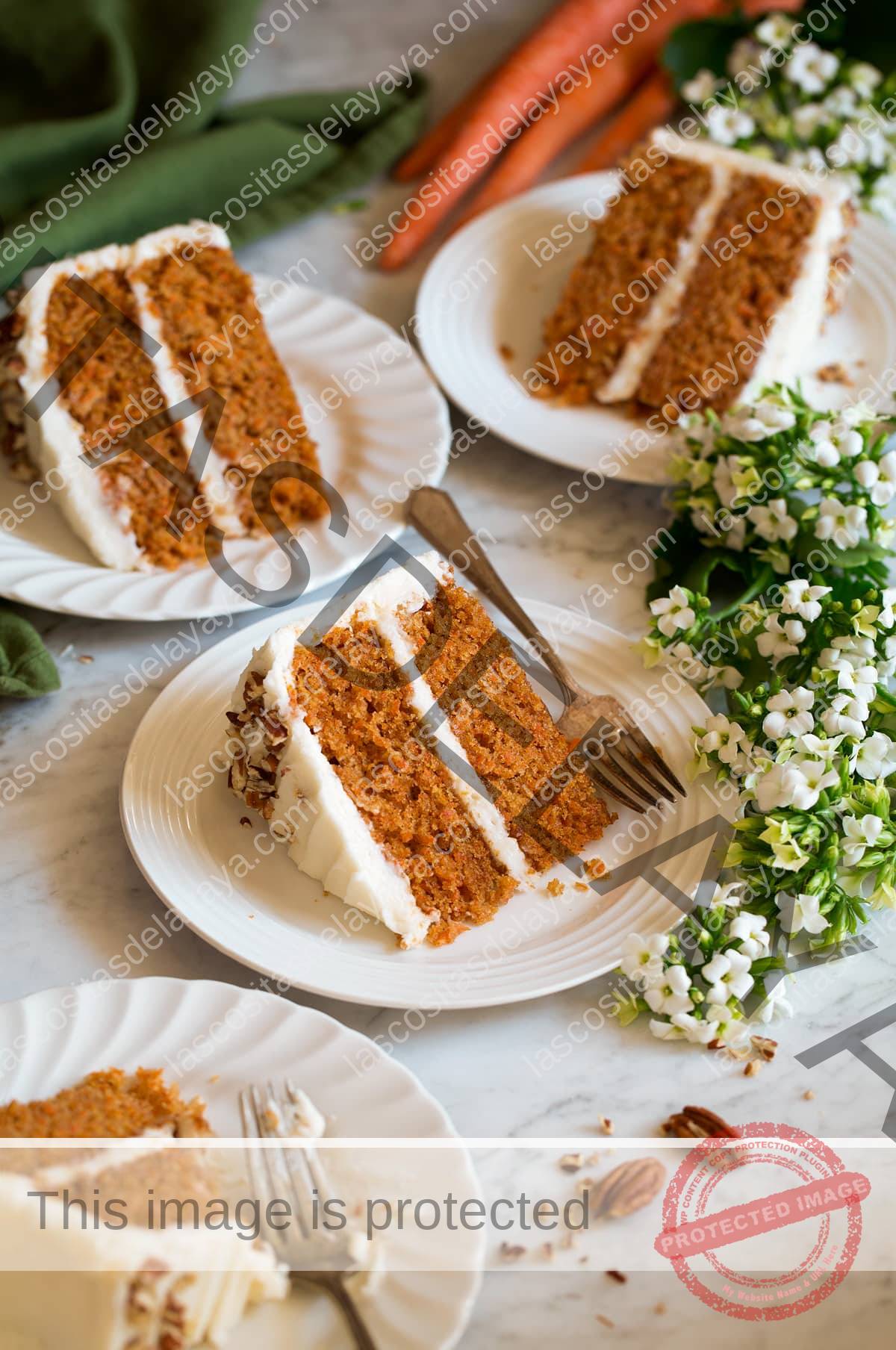 Quatro fatias de bolo de cenoura mostradas em pratos de sobremesa recortados brancos com flores e cenouras ao redor dos pratos.