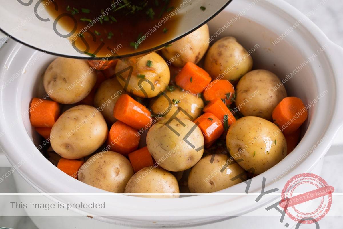 Agregue las papas y las zanahorias sobre la carne asada y vierta sobre la mezcla de caldo.