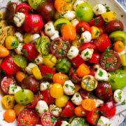 Ensalada de tomate en un cuenco blanco. En la ensalada están los tomates cherry y uva multicolores, las perlas de mozzarella y se cubre con un aderezo de hierbas.