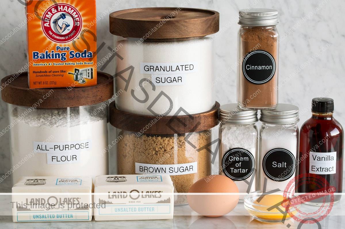 Imagen de los ingredientes utilizados para hacer las galletas Snickerdoodle. Incluye harina, azúcar granulada, azúcar morena, huevo, yema de huevo, mantequilla, sal, crémor tártaro, canela, vainilla y bicarbonato de sodio.