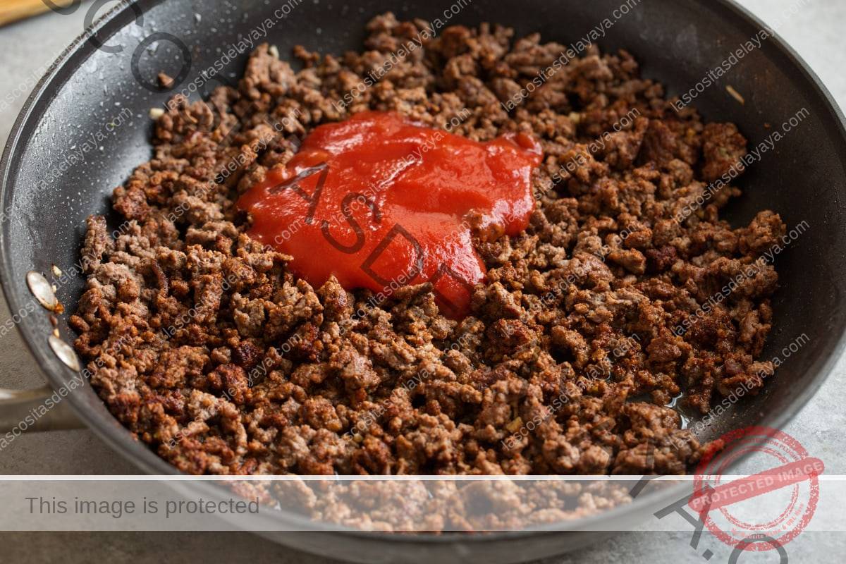 Agregue la salsa de tomate y el caldo de pollo al relleno de carne de taco en la sartén.