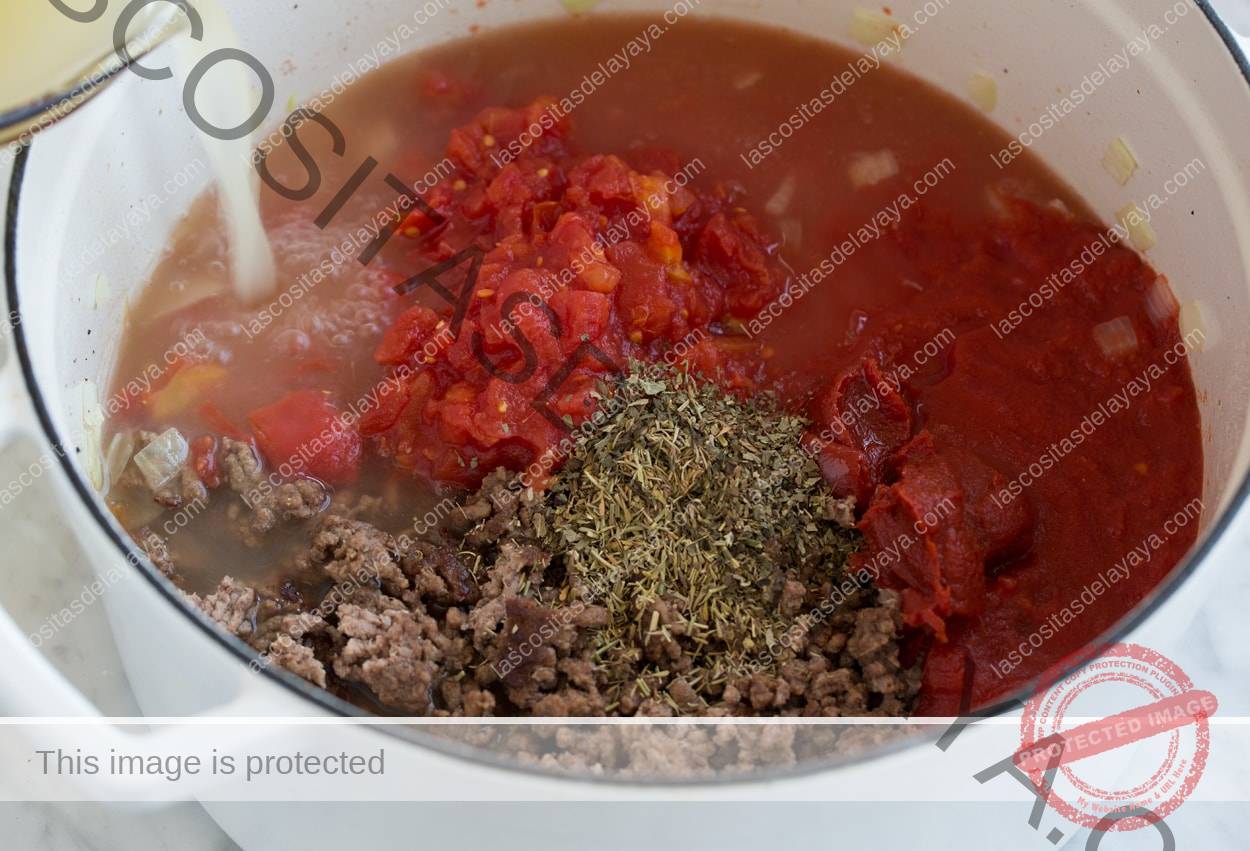 Agregue caldo, tomate y hierbas a la sartén para la sopa de lasaña.