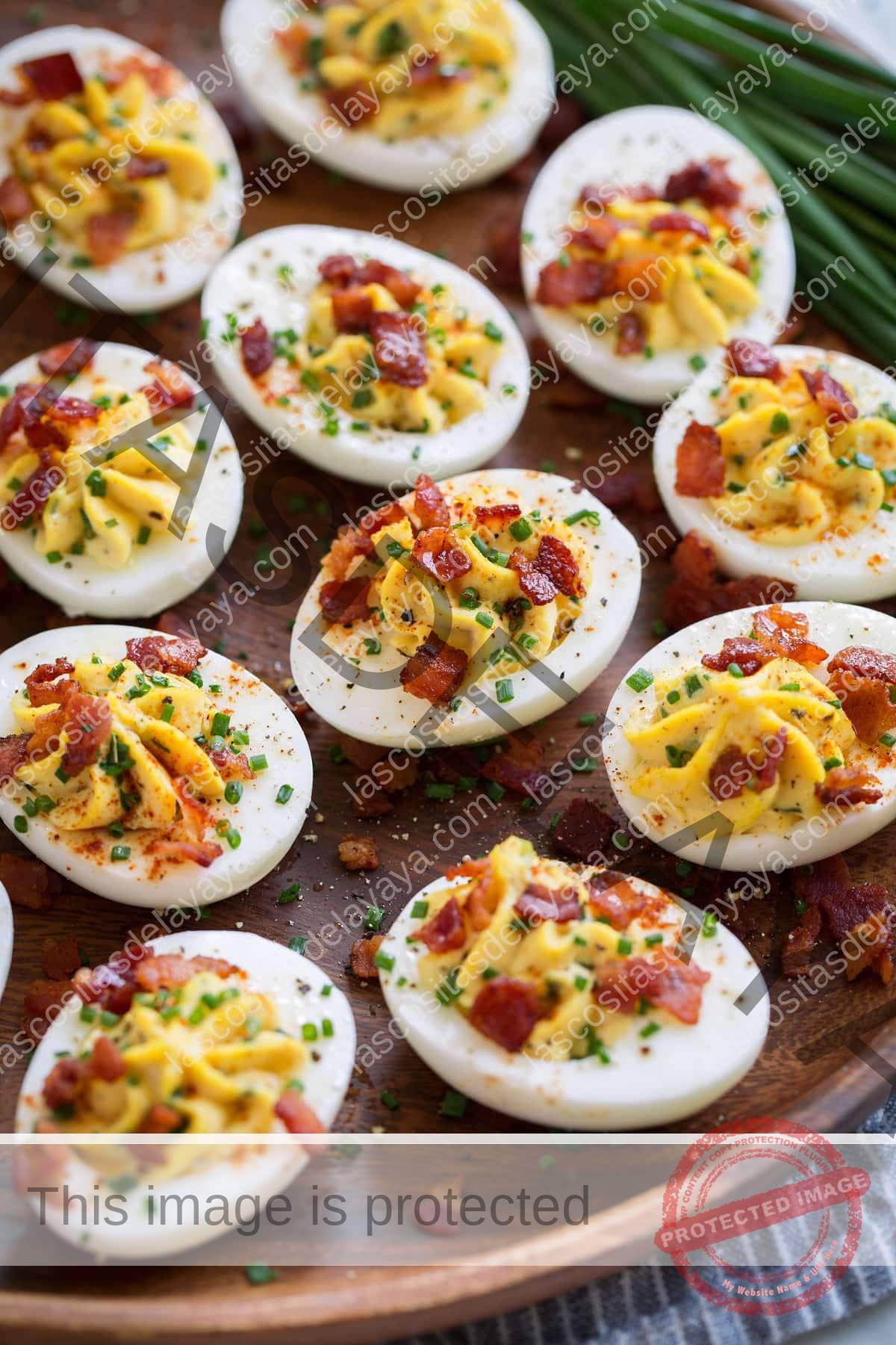 Plato de madera lleno de huevos duros. Huevos rellenos de mayonesa cremosa y relleno de yema de huevo, acompañados de cebollino y tocino.