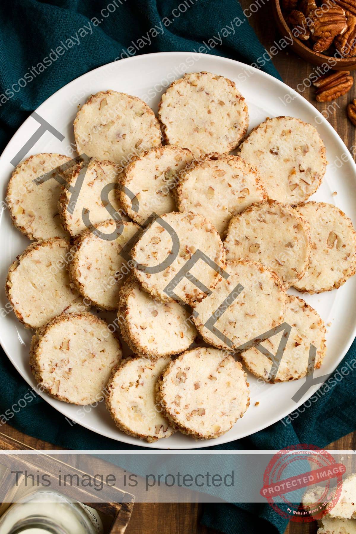 Imagen aérea de galletas de nuez de queso crema apiladas en un plato blanco sobre un paño azul.